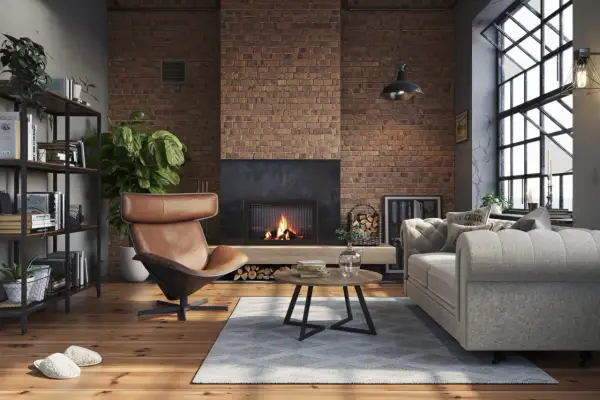 Przytulny, **soft loft** z ceglaną ścianą, palącym się kominkiem, wygodną kanapą i fotelem.